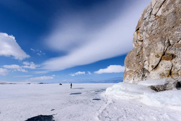 A silhueta do homem está perto do cabo Burhan na rocha de Shamanka na ilha de Olkhon coberta com icicles no dia ensolarado da marcha. Lago Baikal com belas nuvens — Fotografia de Stock