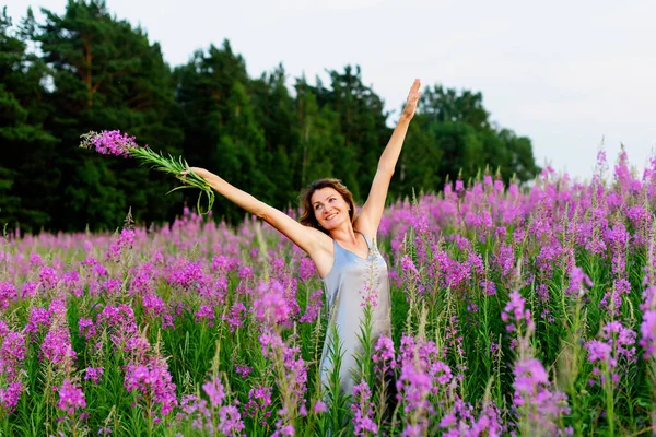 Beautiful woman in gray dress rejoices with her hands up and bunch of flowers on fireweed meadow — Stock Photo, Image