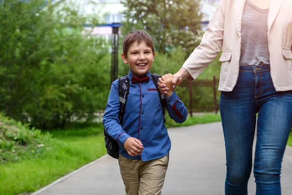 Rodiče a žáci základní školy jdou ruku v ruce. Žena a chlapec s batohem za zády. — Stock fotografie