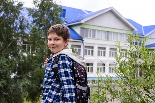 Chlapec s taškou zůstane poblíž základní školy a podívá se do kamery — Stock fotografie