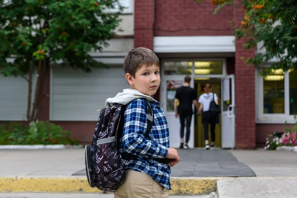 Kind jongen met tas blijft in de buurt van basisschool en kijkt naar de camera — Stockfoto