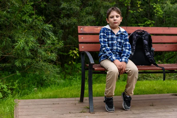 Smutný školní chlapec s batohem sedí na lavičce a přemýšlí — Stock fotografie