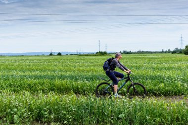 Mutlu fitness kızı bulutlu bir günde yeşil alanda bisiklet sürüyor.