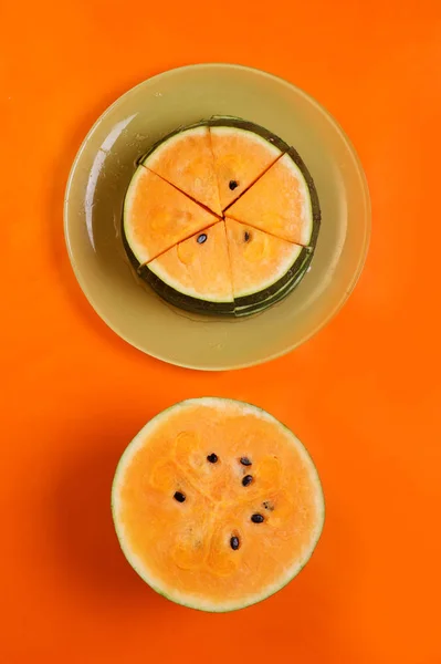 Mitad de sandía fresca de naranja madura y rebanadas en el plato alrededor — Foto de Stock