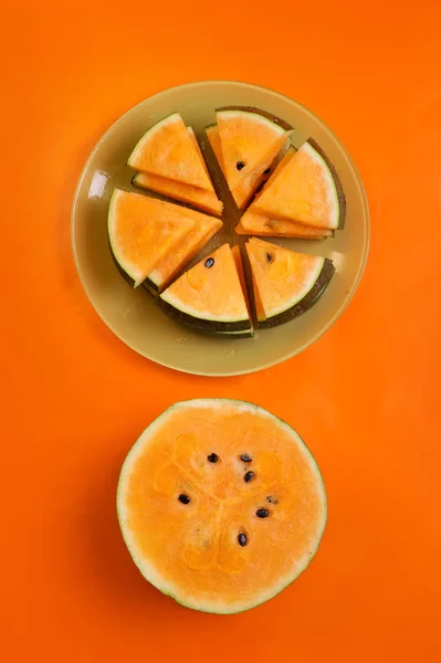 Mitad de sandía fresca de naranja madura y rebanadas en el plato alrededor — Foto de Stock