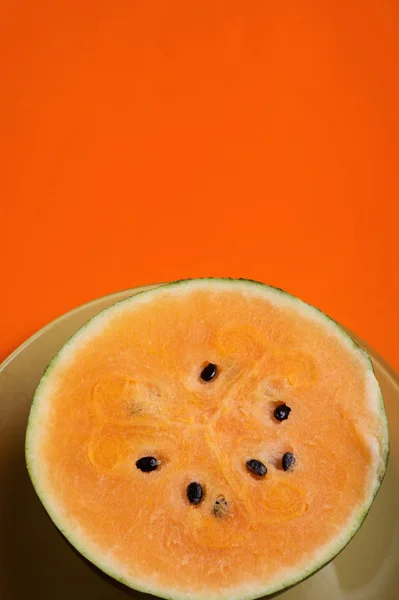 Половина свежего спелого оранжевого арбуза на зеленой тарелке вокруг орана — стоковое фото