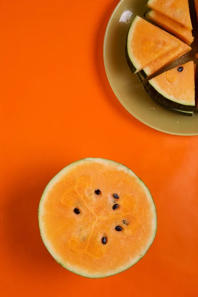 Metade da melancia de laranja madura fresca e fatias na placa ao redor — Fotografia de Stock