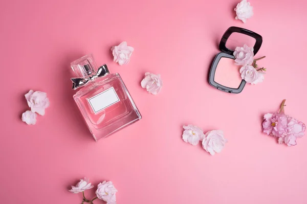 Пляшка парфумів з м'яким рожевим рум'янцем навколо квітів на рожевому — стокове фото