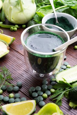 Sebzelerin etrafında spirulinayla detoks yeşil kokteyli. Yaşam tarzı konsepti. Tahta masada çeşitli taze sebzeler.. 