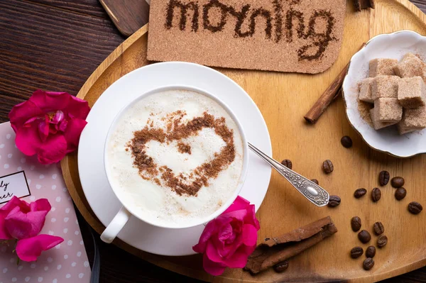 porcelain cup of coffee with ice cream and cinnamon heart served  at black wooden table with pink roses. life style concept