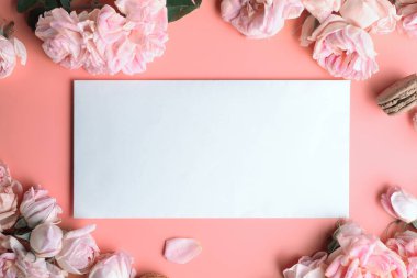 Beyaz zarflı pembe güller ve pembe arka planda badem kurabiyeleri. yaşam tarzı konsepti