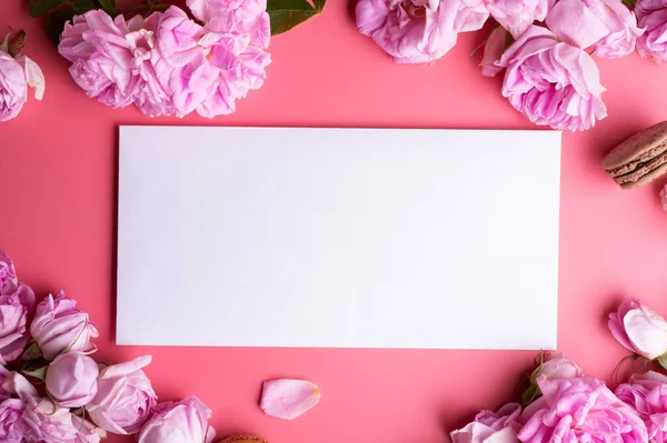 Beyaz zarflı pembe güller ve pembe arka planda badem kurabiyeleri. yaşam tarzı konsepti