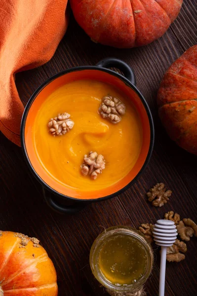 baked pumpkin cream coup with, walnuts ,  coconut milk and natural honey served in nice bowl. served at wooden brown table with ripe orange  pumkins. flat lay. healthy life concept