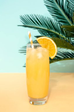 Bardak taze portakal suyu ve yeşil palmiye pastel arka plan üzerinde bırakır. Pop sanat tasarım, en az yaz konsepti. Vintage Photoshop tonlama.