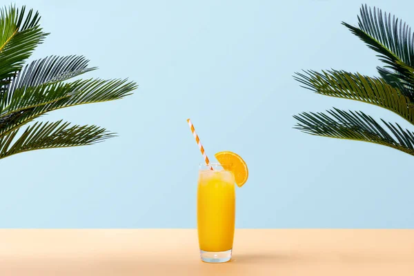 Bardak taze portakal suyu ve yeşil palmiye pastel arka plan üzerinde bırakır. Uzay kopyalayın. Pop sanat tasarım, en az yaz konsepti. Afiş.