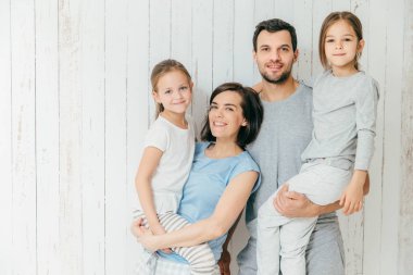 Mutlu aile portresi, güzel kızları ellerinde taşırlar. Güzel beyaz arka plan karşı birlikte dört poz ailen olumlu ifadeler. Sevgi dolu anne ve baba çocukları ile