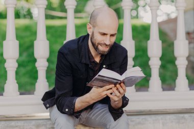 Yakından atış odaklı çekici kel gencin kitap tutan, sevinçle okur, hafta sonları sahiptir, yaz bahçede serbest zaman harcıyor, sakin atmosferi okuma seviyor. İnsanlar ve kavram rahatla.