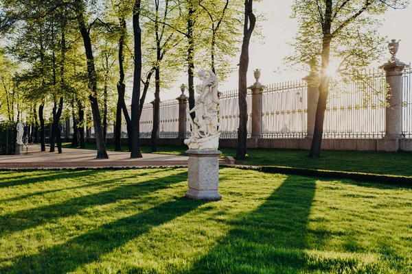 Outdoor shot of Summer Garden in Saint Petersburg. Peace and Victory sculpture. Beautiful view with green lawn, sunshine and grille in background. Places of entertainment in Russia