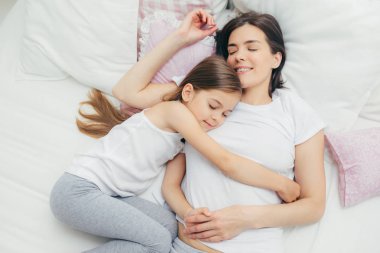 Üstten görünüm neşeli Anne annem büyük bir sevgi ile kucaklayan, iyi tutum gösterir, tatlı rüyalar ve güzel dinlenme hakkına sahiptir, pijama giyiyor kızı yakınındaki beyaz yatakta uyuyor. İnsanlar, kavram uyku