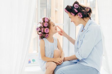 Genç ve güzel anne ve kızı ile curlers saç, iyi ruh hali içinde olmak yatay çekim evde zaman zevk, tatil için hazırlanın. Mutlu aile kavramı. Güzellik, çocuk ve moda kavramı