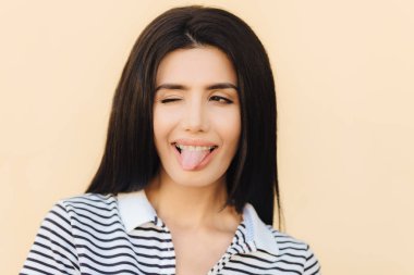 Komik neşeli esmer erkek dil, göz ile yanıp söner gösterir yapar yüz buruşturma, diş teli takıyor, uzun düz siyah lüks saçlı kayıtsızca, ışık arka plan üzerinde izole giyinmiş. İnsanlar ve mutluluk