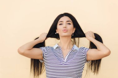 Güzel genç beyaz kadın onun uzun düz siyah saçlı gösterir, dudakları Gücenmek, doğal güzellik, pozlar karşı açık renkli çizgili tişörtlü giyinmiş gösterir. Saç Bakımı ve güzellik kavramı
