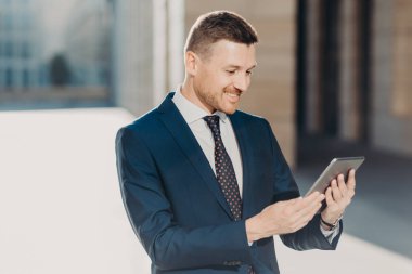 Neşeli erkek Yöneticisi bildirim dijital tablet okur, kravat, kablosuz Internet bağlantısı ile resmi siyah takım elbise giyer, web sayfasında video izliyor. İş ve modern teknolojileri kavramı