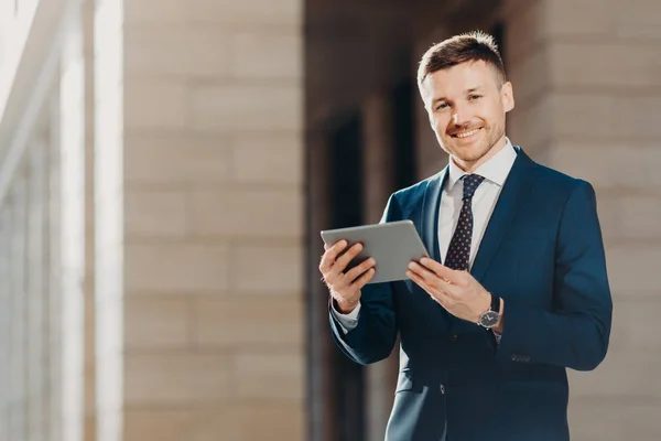 Mutlu erkek girişimci resmi siyah takım elbise giyer, modern tablet bilgisayar tutar, kablosuz internet'e bağlı ağlar, finans haberleri denetler, iş toplantı mali rapor hazırlar
