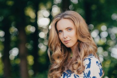 Mavi gözleri ve hafif dalgalı saç çok kadın, pozlar yeşil arka planı açık kamera çekici görünüm ve sağlıklı cilt, ciddi göz vardır. İnsanlar, eğlence ve güzellik kavramı