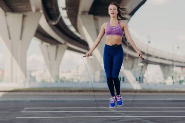 Sportif güzel genç kadın mor üst ve spor ayakkabı, yatay shot atlama ipi tutan, atlama egzersiz açık mı, fitness trianing sabah vardır. Kadınlar, spor ve motivasyon kavramı