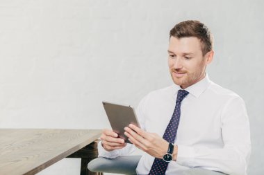 Kişi ve iş kavramı. Resmi kıyafet kullanır dokunmatik yüzey internet, ofis, kablosuz internet'e bağlı olarak finansal haber okuma için genç işadamı beyaz duvara teşkil etmektedir. Adam bankacı