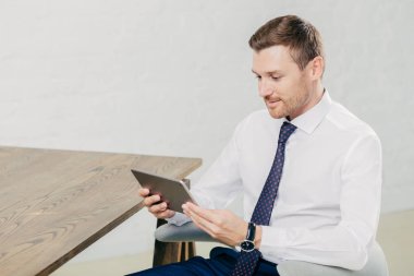 Resmi kıyafetler işadamı konsantre yana shot modern tablet bilgisayar tutar, veri veya e-posta kutusunda, kablosuz internet'e bağlı modern geniş dolapta oturur denetler. İş kavramı