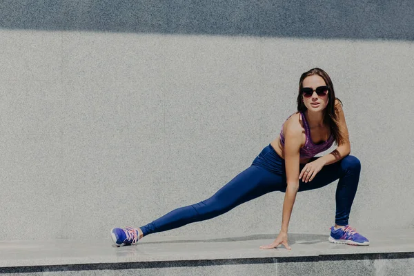 ジョギングやフィットネスの概念 若いアクティブな女性 Exrcices を実行する前に脚の筋肉を伸ばす 毎朝スポーツのために行く フィットして 健康でありたい 色合い 紫のトップスとレギンスを着ています — ストック写真