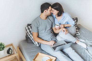 Güzel romantik çift öpecek, birbirlerini yatağa, filmleri izlemek için kullanma dizüstü bilgisayar otururken bakmak, kahve içmek, beraberlik ve dinlenme odasında keyfini çıkarın. İlişki kavramı