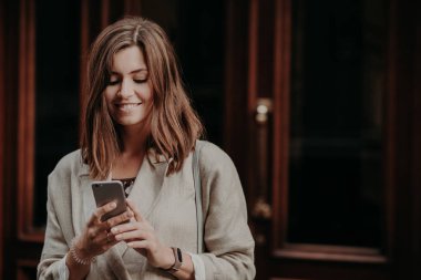 Çok şirin esmer kadın modeli yatay atış cep telefonu, zarif elbiseleri giymiş üzerinden çoklu ortam dosyalarını hisse olumlu haberlerin etkisiyle kablosuz internet'e bağlı internet sitesi, okur.