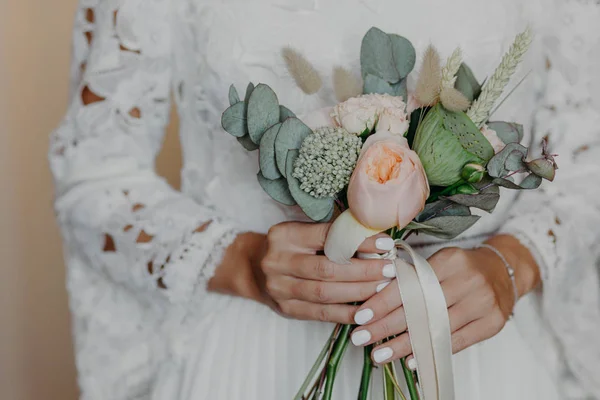 Unrecognizable bride with tender manicure, holds beautiful bouquet, wears white wedding dress. Special occasion, ceremony concept