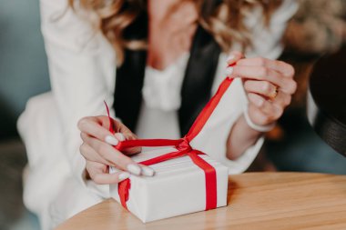 El ile ihale manikür sarılmış hediye kutusu, genç kadının o aldı ne hediye görmek istiyor. Yay, ahşap masa üzerinde tanınmayan kadın bağları. Tatil dekorasyon. Kız ellerinde parsel