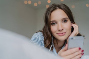 Oldukça koyu saçlı kadın spneds serbest zaman en sevdiği şarkıyla samimi shot modern cep telefonu tutan, doğrudan kameraya benziyor, kapalı teşkil etmektedir, yapmak vardır. Çekici kız yeni melodiler arar
