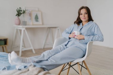 Rahat Erkek pijama, giyinmiş kapalı atış sandalyeye oturur, bacaklarını yatağa tutar, sıcak kahve içer, karşı iç iç teşkil etmektedir, çekici bir görünüme sahiptir. İnsanlar, dinlenme ve rahatlama kavramı