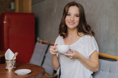 İhale gülümsemeyle gülümseyen kadın fincan çay ya da kahve tutar, iyi dinlenme sahiptir, rahat kafe ya da restoran teşkil etmektedir, arkadaş, gündelik kıyafeti giymiş bekler. İnsanlar, dinlenme ve yaşam tarzı kavramı