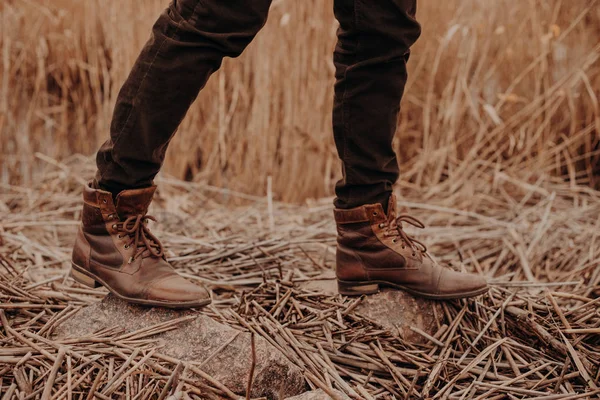 Cropped shot of unrecognizable man wears old leather brown footwear, poses on ground with stubble, walks at field alone.