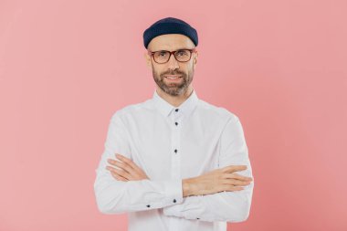 Kendi kendine güvenen tıraşsız adamın kapalı atış kameraya mutlu görünüyor, katlanmış silah tutar, şapkalar ve gömlek giyer, muhatap, pembe bir arka plan üzerinde izole dikkatle dinler. Erkeklik kavramı