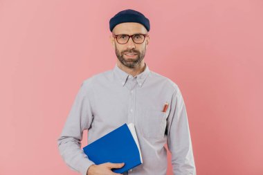 Görüntü kendini genç erkek ile anız, şeffaf gözlük takar, ders kitabı kol altında tutar, proje çalışması hazırlar, pembe bir arka plan karşı modelleri emin. Not defteri pozlar kapalı ile işadamı.