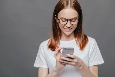 Güzel kadının neşeli ifade ile resim kırpılmış, gülümsüyor geniş, tutar ile kopya alanı sol tarafında gri arka plan karşı cep telefonu, erkek arkadaşından, mesaj almak için mutlu duruyor