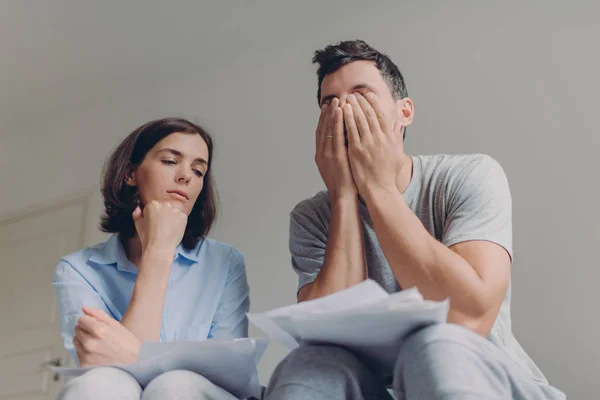 Stressful family couple have debt problems, not able to pay their loan, manage domestic budget, study paper documents, pose together, wear casual clothes. Husband and wife review bank account