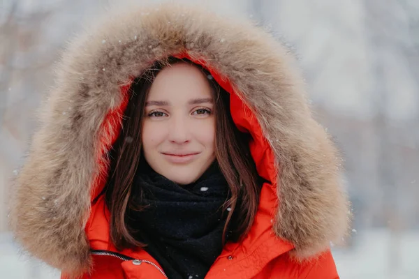Close-up shot van aantrekkelijke vrouw draagt rode vest met hoody, sjaal, wandelingen buiten tijdens frosty winterweer, geniet van vrije tijd kijkt direct naar de camera. Mensen, seizoen en recreatieve concept — Stockfoto