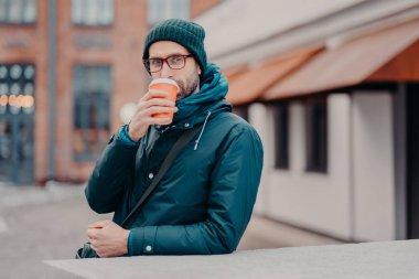 Yakışıklı hipster açık atış tek kullanımlık Kupası başlık içinde giyinmiş, takeawy kahve içer, ceket, gözlük takıyor, srtoll dışında kamera düz göz vardır. İnsanlar ve yaşam tarzı
