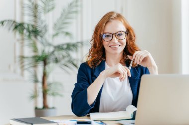 Mutlu redhaired kadın çalışan optik gözlük, portresi memnun ifade, modern araçlar ile çalışır, meslektaşım ile toplantı için bekler, muhasebe raporunu hazırlar, kendi dolapta oturur