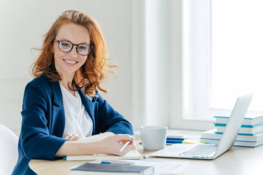 Kendi kendine güvenen genç kadın yönetmen iş süreci planları, Not Defteri'nde ana Tezler yazar, dizüstü bilgisayar bilgileri yeniden yazar, çay içer, ofis iç üzerinde teşkil etmektedir. Teknoloji, meslek