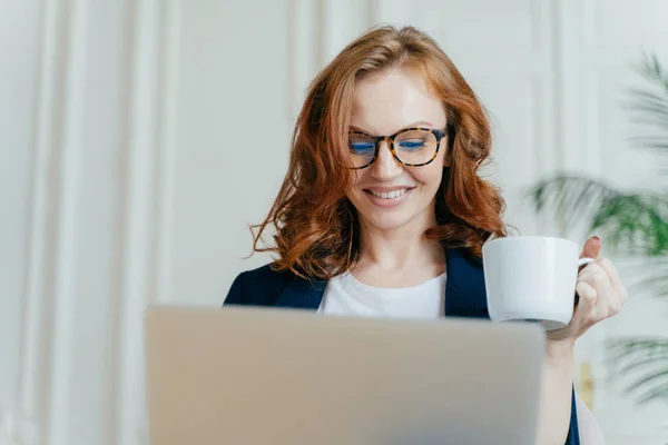 Optik Gözlük, headshot gülümseyen, kırmızı saçlı kadın sahiptir sıcak kahve veya çay, dizüstü bilgisayar, odaklı satın alma online, gülümsüyor hoş yapar, mesafe, kitap bilet serbest inşaat